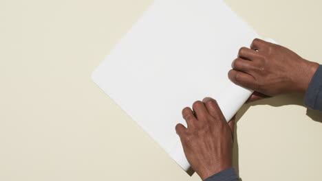 Video-Von-Händen-Eines-Afroamerikanischen-Mannes,-Der-Weißes-Papier-Auf-Weißem-Hintergrund-Aufrollt