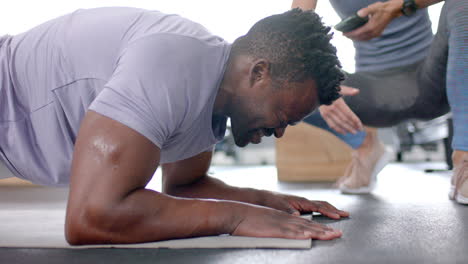 Fit-African-American-man-doing-push-ups-at-the-gym-with-a-trainer