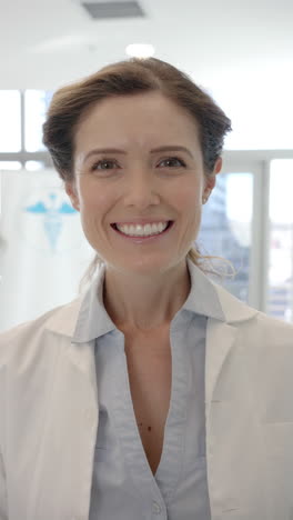 Vertical-video-portrait-of-caucasian-female-doctor-smiling-in-hospital-corridor,-slow-motion