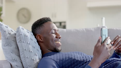 Glücklicher-Afroamerikanischer-Mann-Mit-Smartphone-Und-Kreditkarte-Im-Sonnigen-Wohnzimmer,-Zeitlupe