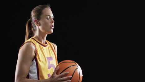 Young-Caucasian-woman-holds-a-basketball-on-a-black-background,-with-copy-space