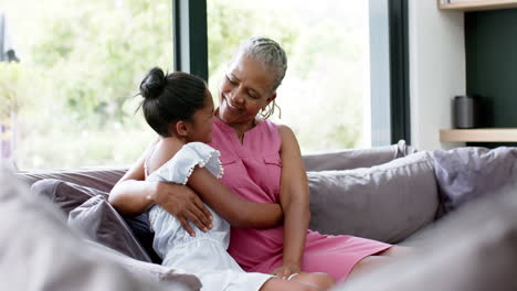 Happy-african-american-granddaughter-and-grandmother-hugging-on-sofa,-copy-space,-slow-motion