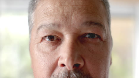 Portrait-close-up-of-opening-eyes-of-senior-biracial-man-smiling-at-home,-slow-motion