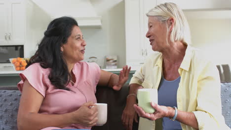 Happy-diverse-senior-women-with-coffee,-discussing,-laughing-in-sunny-living-room,-slow-motion