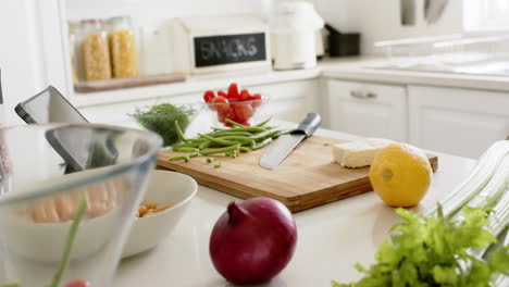 Knife,-cutting-board,-vegetables-and-tablet-on-counter-in-sunny-kitchen,-slow-motion