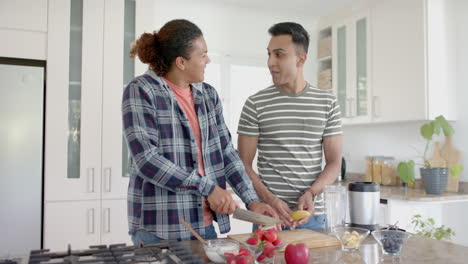 Happy-diverse-gay-male-couple-cutting-fruit-for-healthy-smoothie-in-kitchen,-slow-motion