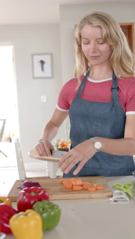 Vertical-video-of-portrait-of-happy-caucasian-woman-cutting-vegetables-in-kitchen,-slow-motion