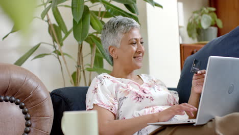 Glückliche-ältere-Frau-Mit-Gemischter-Abstammung,-Die-Auf-Der-Couch-Sitzt-Und-Zu-Hause-Einen-Laptop-Benutzt,-Zeitlupe