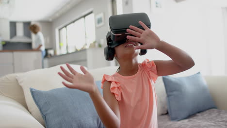 Happy-biracial-girl-wearing-vr-headset-using-virtual-interface-in-living-room,-slow-motion