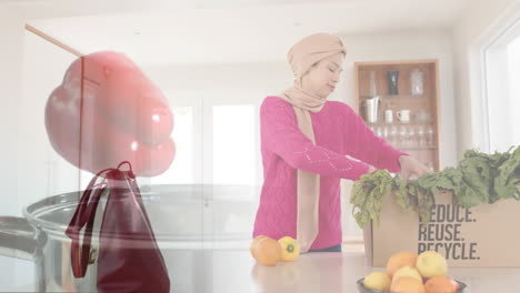Mujer-Birracial-En-Hijab-Con-Caja-De-Verduras-En-La-Cocina,-Cocinando-Sobre-Pimiento-Rojo