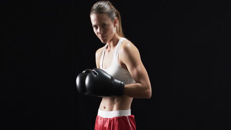 Young-Caucasian-woman-boxer-in-boxing-gear-poses-confidently-on-a-black-background