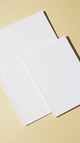 Vertical-video-of-books-with-blank-white-pages-and-copy-space-on-yellow-background