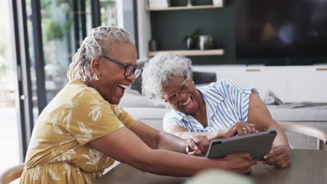 Glückliche-ältere-Afroamerikanische-Freundinnen,-Die-Ein-Tablet-Benutzen-Und-Im-Esszimmer-Lachen,-Zeitlupe