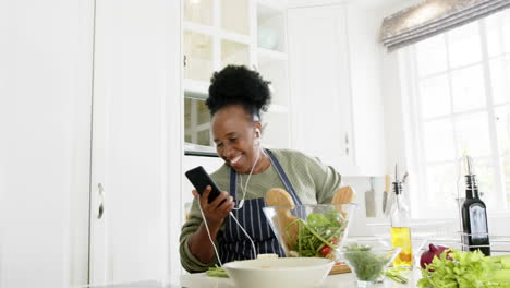 Fröhliche-Afroamerikanische-Seniorin,-Die-Mit-Smartphone-Und-Kopfhörern-In-Der-Küche-Tanzt,-Zeitlupe