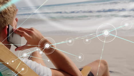 Animation-of-network-of-connections-over-caucasian-man-talking-on-smartphone-at-beach