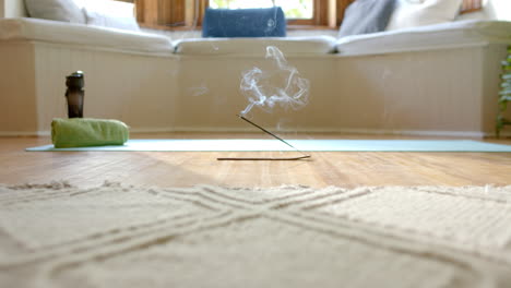 Close-up-of-incense-sticks-with-smoke-trails-on-floor-over-yoga-mat-at-home