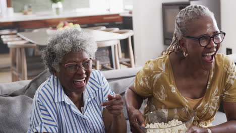 Happy-senior-african-american-female-friends-eating-popcorn,-watching-tv-and-laughing,-slow-motion