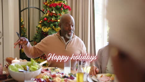 Animation-of-happy-holidays-text-over-diverse-senior-friends-at-christmas-dinner-at-home