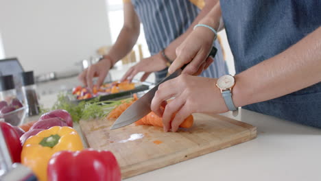 Happy-diverse-couple-preparing-fresh-vegetables-and-wearing-aprons-in-kitchen,-slow-motion