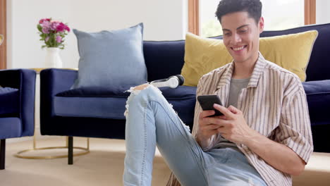 Happy-biracial-man-sitting-on-floor-using-smartphone-in-living-room,-copy-space,-slow-motion