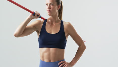 Young-Caucasian-woman-athlete-holds-a-javelin-at-the-gym-on-a-white-background