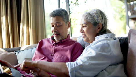 Glückliches,-Abwechslungsreiches-Seniorenpaar,-Das-Zu-Hause-Auf-Der-Couch-Sitzt-Und-Mit-Einem-Tablet-Online-Einkauft