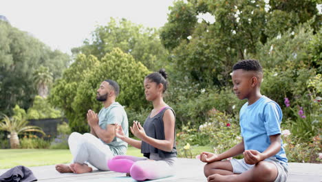 Padre-Afroamericano,-Hijo-E-Hija-Practicando-Meditación-De-Yoga-Sentados-En-El-Jardín,-Cámara-Lenta