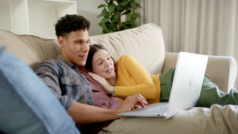 Happy-diverse-couple-sitting-on-sofa-using-laptop-at-home,-in-slow-motion