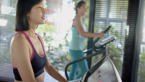 Happy-asian-female-friends-exercising-and-smiling-in-sunny-home-gym,-slow-motion