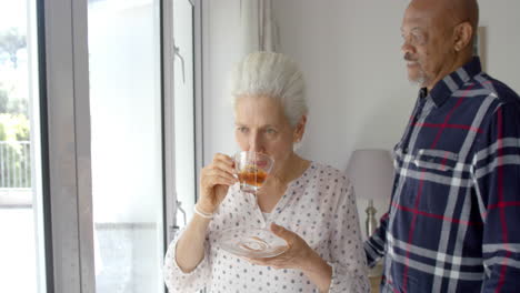Glückliches-älteres-Biracial-Paar,-Das-Tee-Trinkt-Und-Sich-Zu-Hause-Umarmt,-Zeitlupe