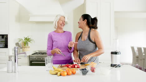 Zwei-Glückliche,-Vielfältige-Seniorinnen-Hacken-Obst-Und-Lachen-In-Einer-Sonnigen-Küche,-Zeitlupe