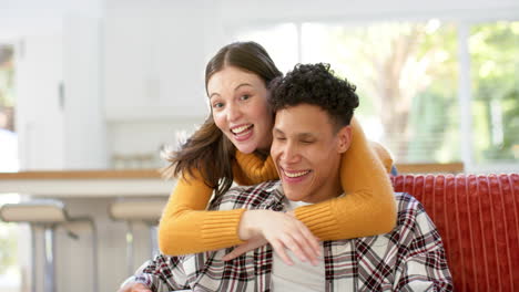 Portrait-of-happy-diverse-couple-sitting-on-sofa-and-embracing-at-home,-in-slow-motion
