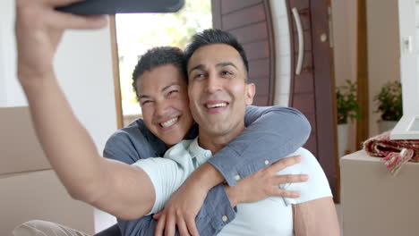 Happy-diverse-gay-male-couple-moving-into-new-home,-taking-selfies-in-living-room,-slow-motion