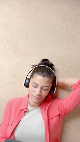 Vertical-video-of-biracial-teenage-girl-on-floor-with-headphones-and-phone,-copy-space,-slow-motion