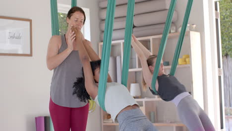 Diverse-fitness-teenage-girls-in-aerial-yoga-class-with-female-coach-in-big-white-room,-slow-motion
