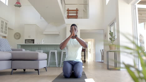 Fokussierter-Afroamerikanischer-Mann-Praktiziert-Yoga-Meditation-Im-Sonnigen-Wohnzimmer,-Zeitlupe