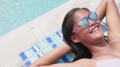 High-angle-of-happy-african-american-girl-in-sunglasses-sunbathing-by-pool,-copy-space,-slow-motion