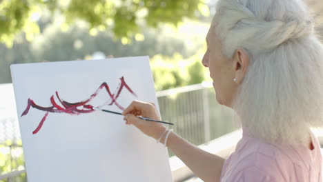 Happy-senior-biracial-woman-painting-at-balcony-at-home,-slow-motion