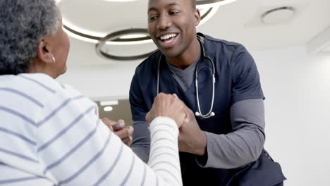 Happy-african-american-male-doctor-holding-hands-of-senior-woman-in-hospital,-slow-motion