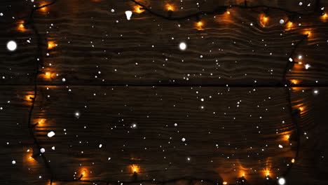 Animation-of-snow-falling-over-fairy-lights-on-wooden-background-with-copy-space-at-christmas