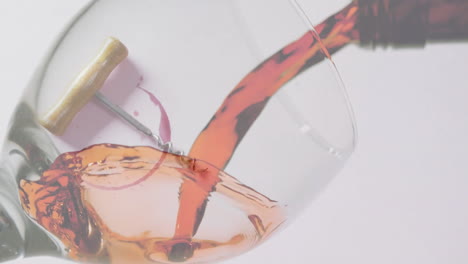 Composite-of-red-wine-being-poured-into-glass-over-corkscrew-on-white-background