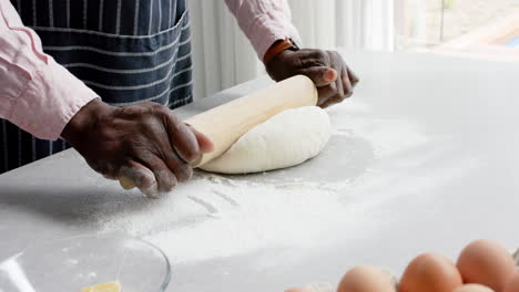 Biracial-man-wearing-apron-baking-and-rolling-dough-in-kitchen,-slow-motion
