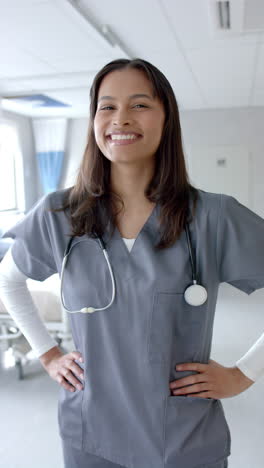 Vertical-video-portrait-of-biracial-female-doctor-smiling-in-hospital-ward,-slow-motion