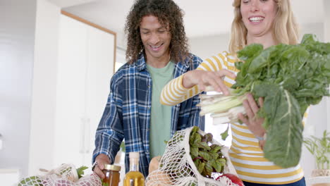 Happy-diverse-couple-unpacking-grocery-shopping-bags-in-kitchen,-slow-motion