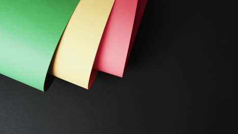 Video-of-rolled-up-red,-yellow-and-green-papers-with-copy-space-on-black-background