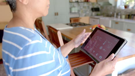 Fokussierte-ältere-Frau-Mit-Gemischter-Abstammung,-Die-Zu-Hause-Ein-Tablet-Mit-Smart-Home-Auf-Dem-Bildschirm-Verwendet