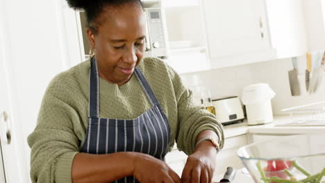 Feliz-Mujer-Mayor-Afroamericana-Preparando-Ensalada-En-Una-Cocina-Soleada,-Cámara-Lenta