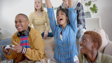 Happy-diverse-group-of-teenage-friends-raising-hands-and-playing-video-games-at-home,-slow-motion