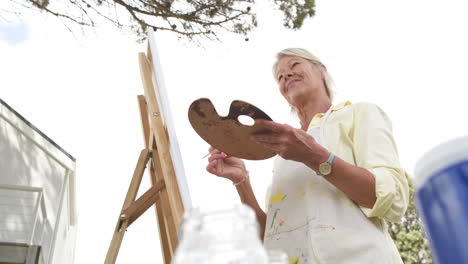 Happy-caucasian-senior-woman-painting-picture-and-smiling-in-sunny-garden,-slow-motion,-copy-space