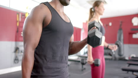 Fit-African-American-man-and-young-Caucasian-woman-exercising-at-the-gym,-lifting-weights